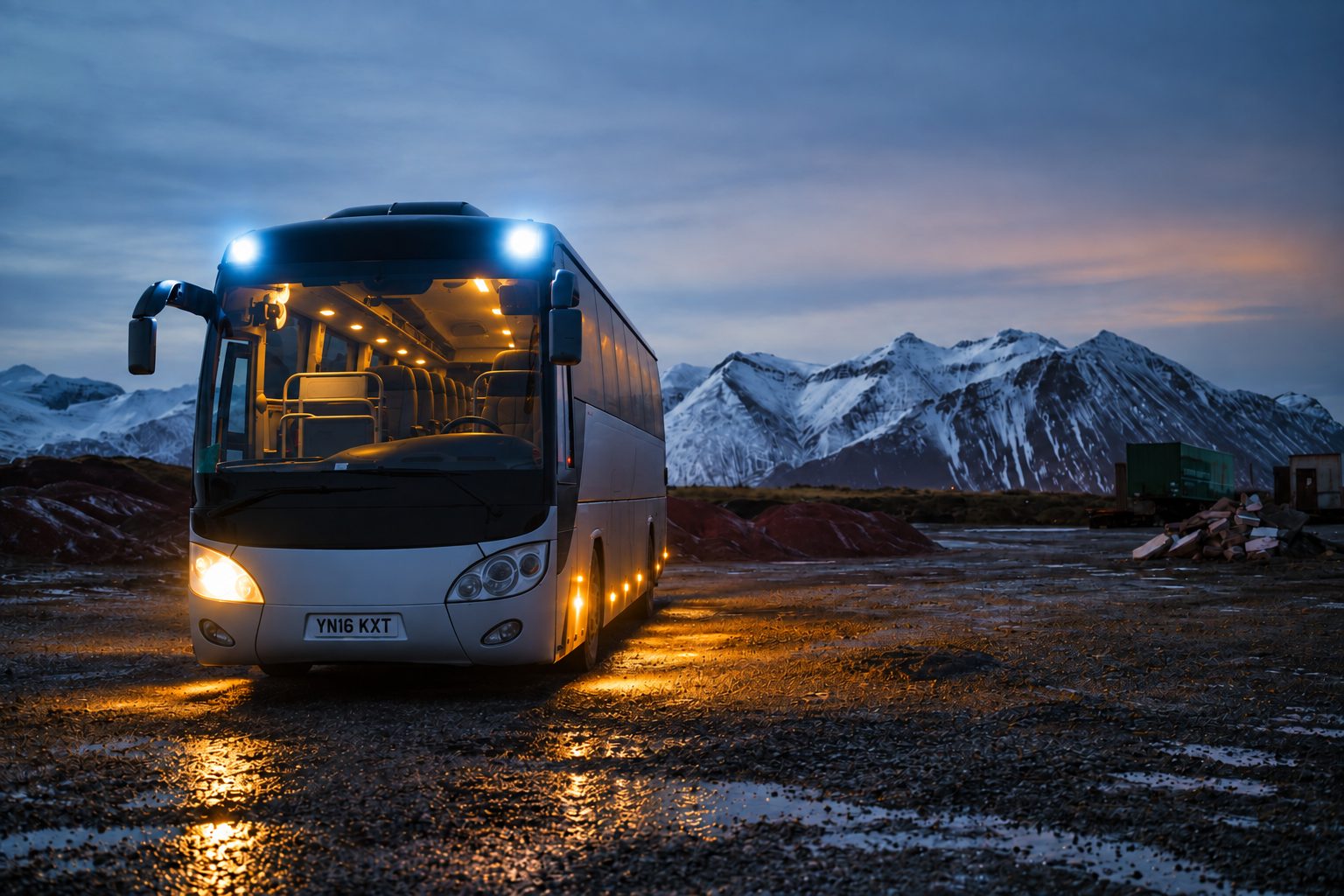 A vehicle with its lights on at dusk in front of mountains